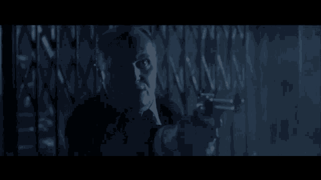 a man in a suit and tie is pointing a gun at someone in a dark room .