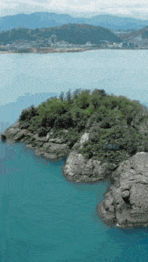 a small island in the middle of a large body of water with mountains in the background