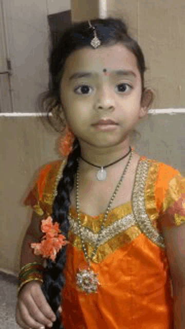 a little girl wearing an orange dress and a necklace