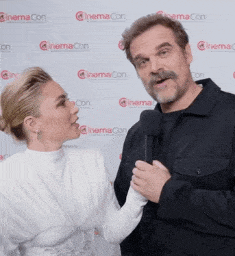 a man and a woman are standing in front of a wall that says cinema con