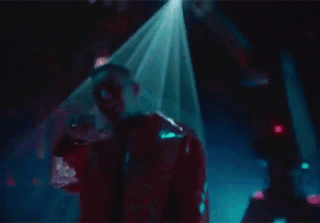 a man in a red jacket is dancing in a dark room with a green light coming out of the ceiling .