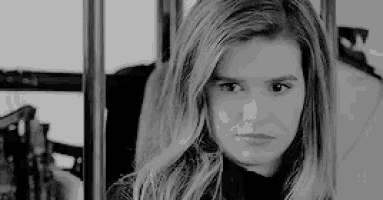 a black and white photo of a woman looking at the camera while sitting on a bus .
