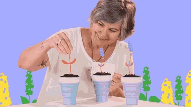 a woman with a tattoo on her arm is watering three potted flowers
