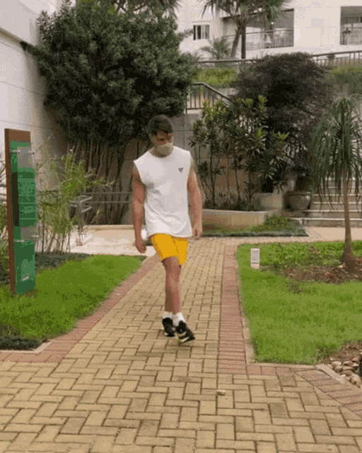 a man wearing a white tank top and yellow shorts walks down a brick path