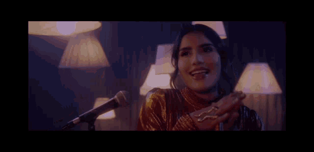 a woman is singing into a microphone in a dark room with lamps in the background .
