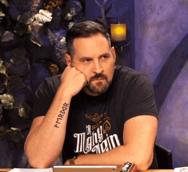 a man with a tattoo on his arm that says pmrror sits at a table