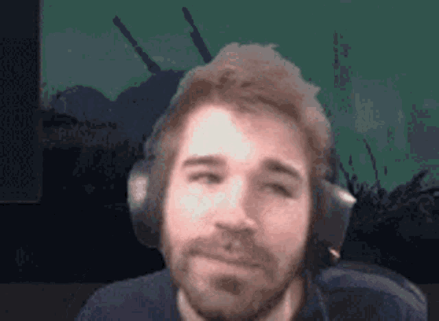 a man with a beard is wearing headphones in front of a green background .