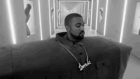 a black and white photo of a man wearing a hoodie and a necklace standing in a hallway .