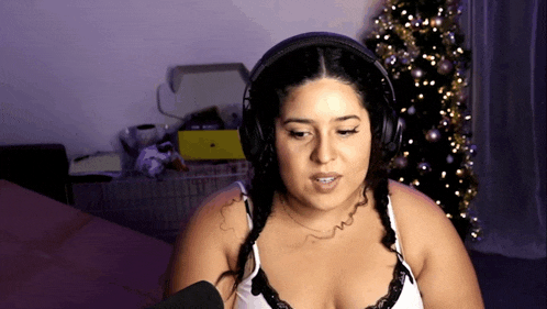 a woman wearing headphones and a bra is sitting in front of a christmas tree