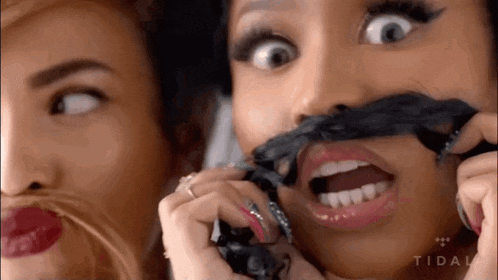 two women are making fake mustaches on their faces while talking on a cell phone .
