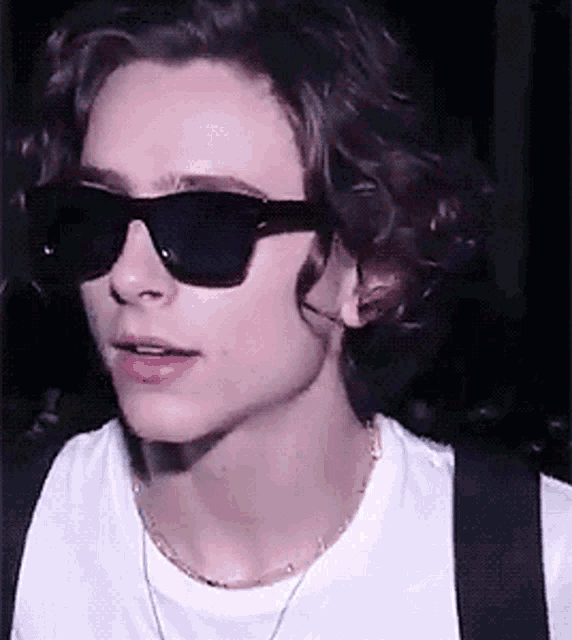 a young man with curly hair wearing sunglasses and a white shirt .