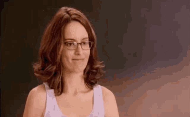 a woman wearing glasses and a tank top is making a funny face .