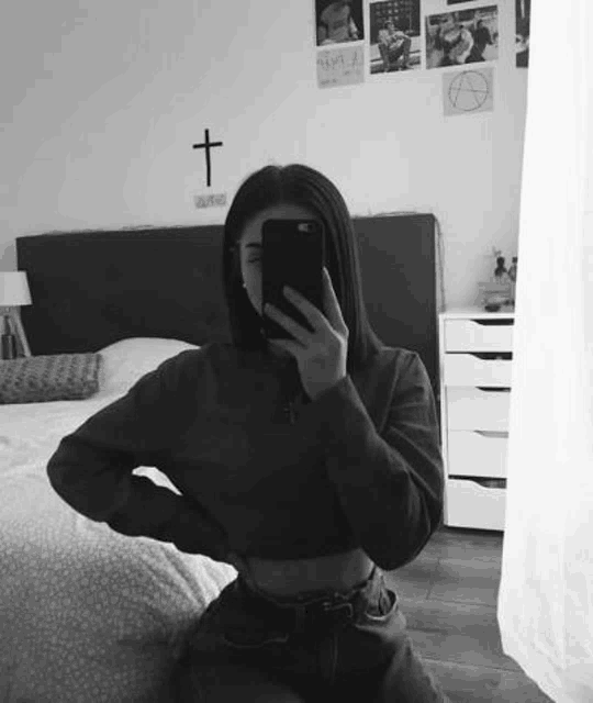 a woman is taking a selfie in a bedroom with her phone .