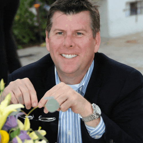 a man in a suit and striped shirt is smiling and holding a pair of glasses
