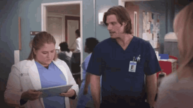 a man and a woman in scrubs are standing next to each other in a hospital room .