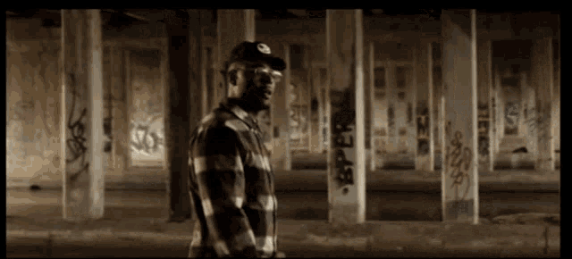 a man in a plaid shirt is standing in an empty building with graffiti on the walls
