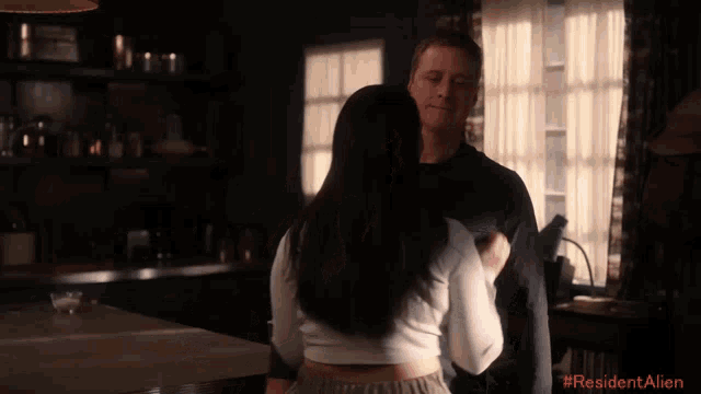 a man and a woman are hugging in a room with #residentalien written in red