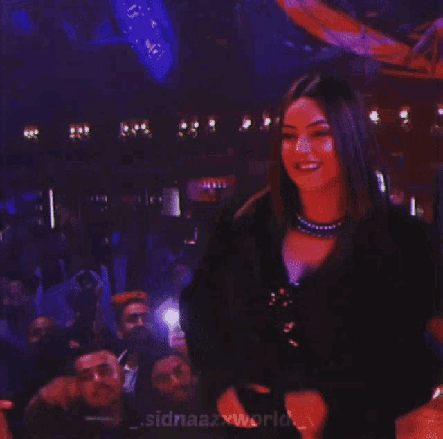 a woman stands in front of a crowd with the words sidnaazxworld on the bottom right