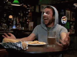 a man wearing a hooded sweatshirt is sitting at a table with a plate of food and a glass of beer