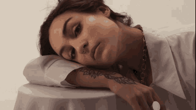 a woman with a tattoo on her wrist rests her head on a table