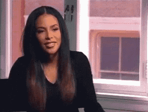a woman with long hair is sitting in front of a window smiling .