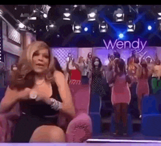 a woman in a black dress is sitting in front of a crowd of people on a stage .