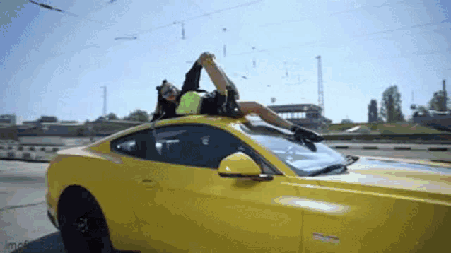 a woman laying on the roof of a yellow car