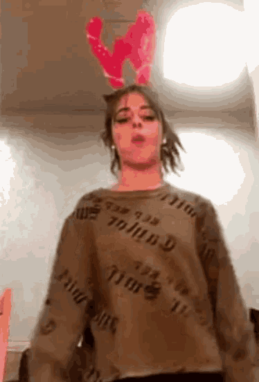 a woman wearing a sweater and antlers is standing in front of a wall .