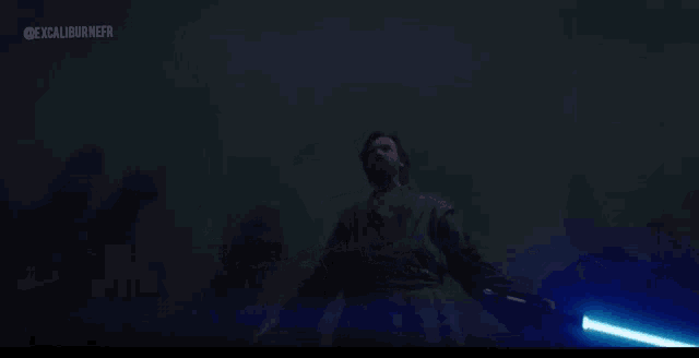 a man with long hair is holding a blue light saber in the dark .