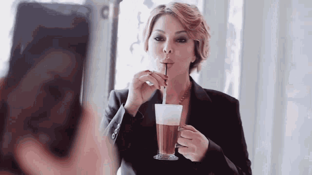 a woman taking a picture of herself drinking a drink through a straw
