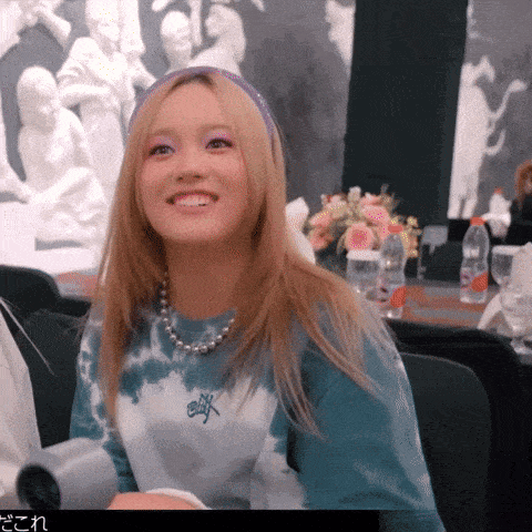 a woman wearing a tie dye shirt and a pearl necklace is smiling