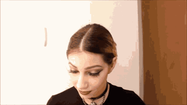 a woman wearing a choker necklace and a black shirt is looking down .