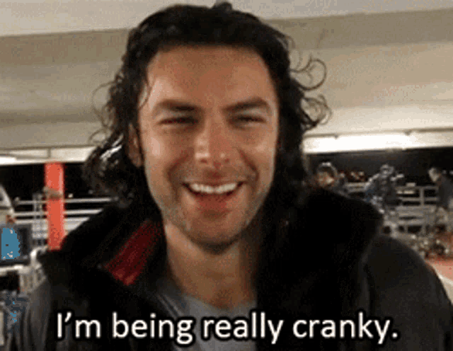 a man with long hair and a beard is smiling and says i 'm being really cranky