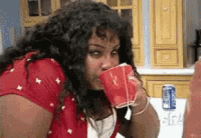 a woman in a red shirt is drinking from a red cup in a kitchen