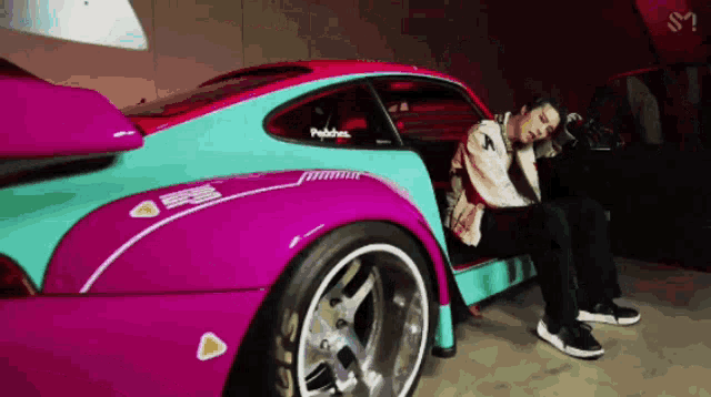 a man sits in the doorway of a pink and blue sports car with a sticker on the side that says productions