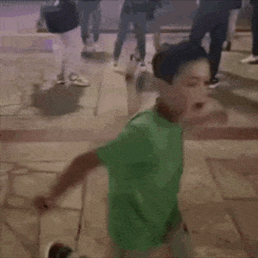 a young boy in a green shirt is dancing on a stone floor .