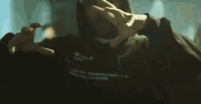 a man in a hoodie is making a peace sign with his hands in a blurry photo .