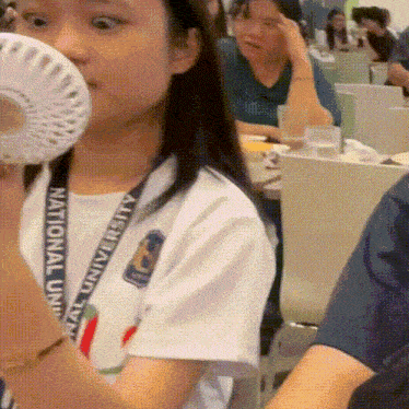 a woman wearing a national university lanyard is holding a fan