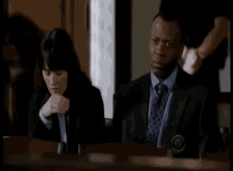 a man in a suit and tie is sitting at a table with a woman covering her face .