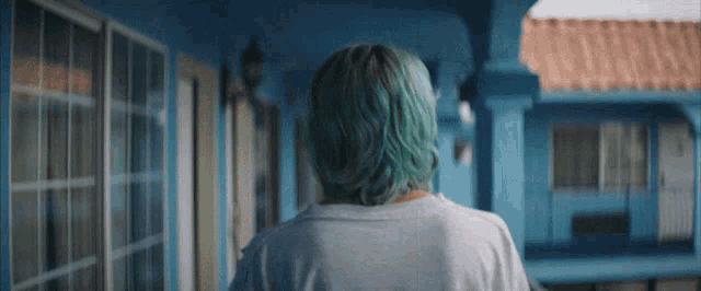 a woman with blue hair is walking down a hallway in front of a blue building