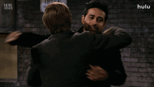 two men hugging in front of a brick wall that says hulu on it