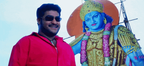 a man in a red shirt stands next to a blue statue