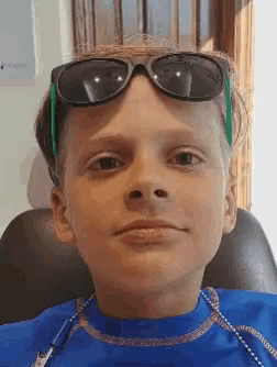 a young boy wearing sunglasses and a blue shirt is sitting in a chair