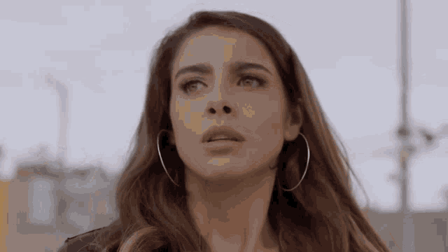 a woman wearing hoop earrings and a leather jacket is looking up .