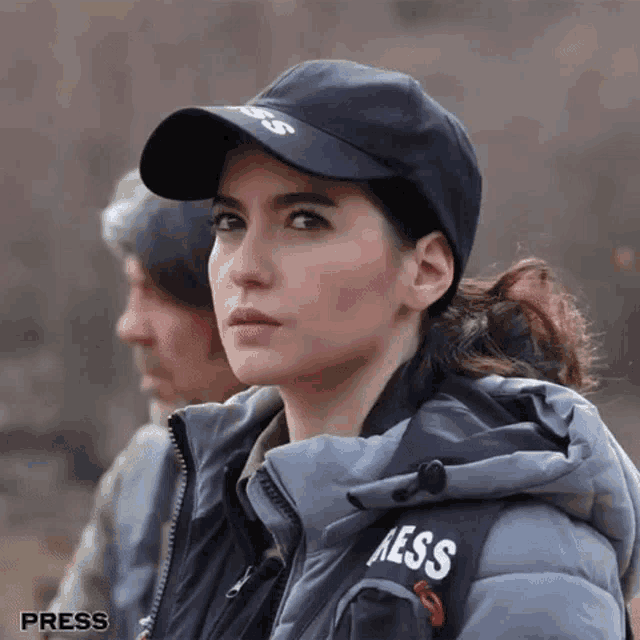 a woman wearing a black hat and a grey jacket that says aess