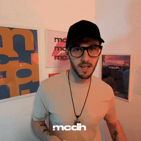 a man wearing glasses and a hat is standing in front of a wall with framed pictures and the word mcdh on the bottom