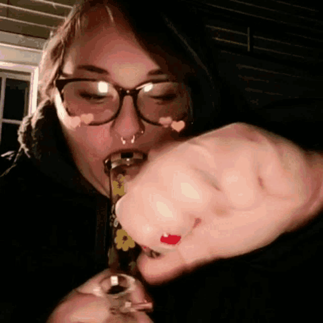 a woman wearing glasses is smoking a bong with flowers on it .