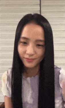 a woman with long black hair is wearing a purple shirt and smiling at the camera .