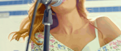 a woman singing into a microphone with a floral top on