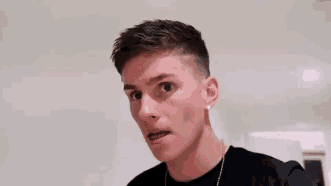 a young man is making a funny face while wearing a black shirt and a gold chain .